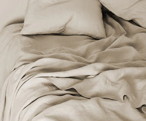 Natural linen sheet set in neutral tone, includes flat sheet, fitted sheet with 100% European flax with deep pockets, and pillowcases – displayed on a neatly made bed.