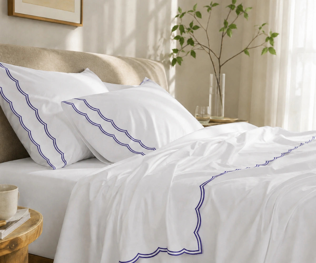 Close-up of white pillowcases and flat sheet featuring a navy blue scalloped embroidered border.
