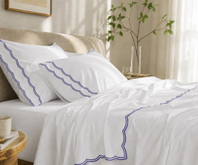 Close-up of white pillowcases and flat sheet featuring a navy blue scalloped embroidered border.
