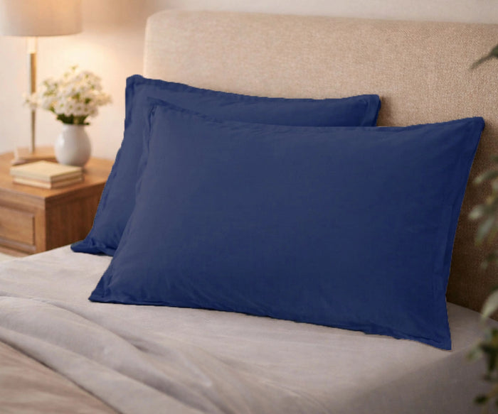 Navy blue organic cotton pillow covers on a modern bed with white sheets and a beige headboard.
