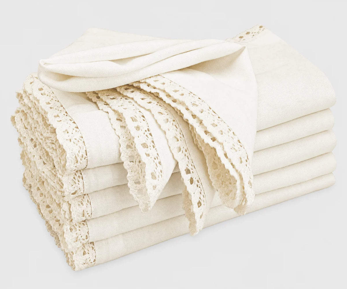 A stack of folded off-white cotton cloth napkins featuring delicate lace trim and cutwork edges
