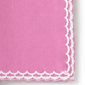 A close-up of a pink fabric napkin with a white scalloped lace border along one corner.