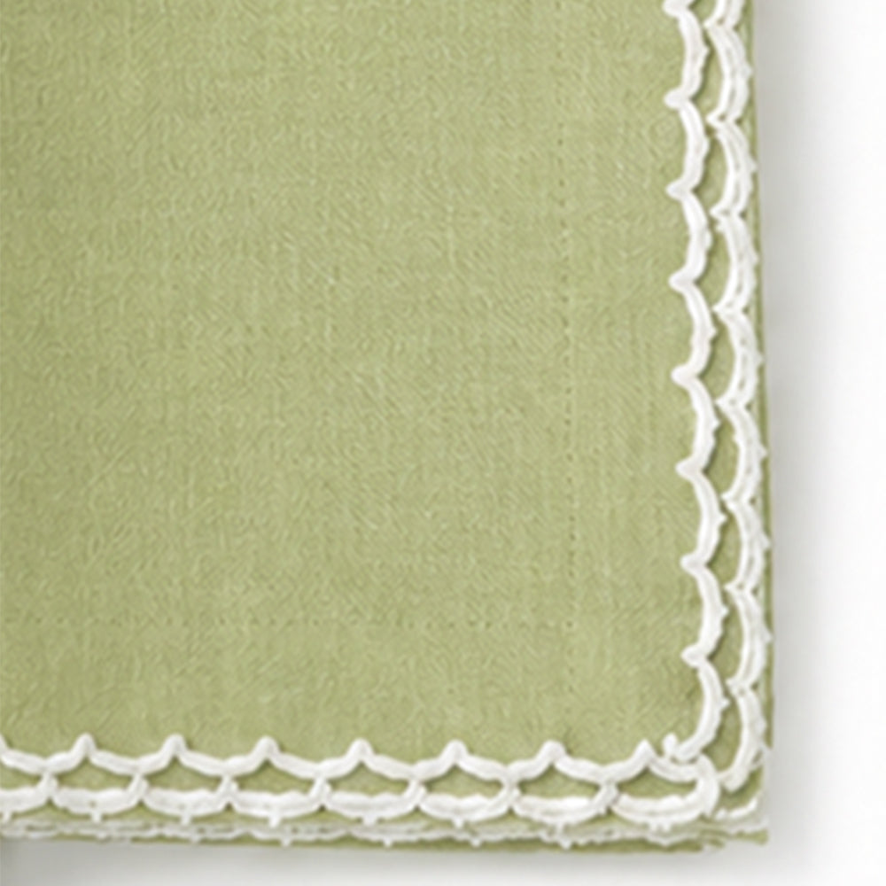 A close-up of a pista green cotton napkin with a white scalloped lace border.