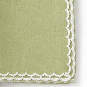 A close-up of a pista green cotton napkin with a white scalloped lace border.