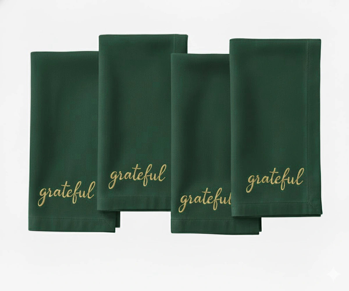 Green cotton napkin with beige “Grateful” embroidered text for holiday tables.