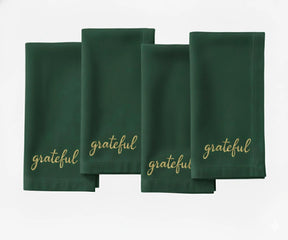 Green cotton napkin with beige “Grateful” embroidered text for holiday tables.