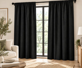 Pair of black plain cotton curtains hanging on a dark rod in a bright living room.