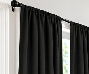 Black curtain panels hanging from a black rod in a window, shown against a white wall and trim.