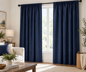 Pair of blue plain cotton curtains hanging on a dark rod in a bright living room.