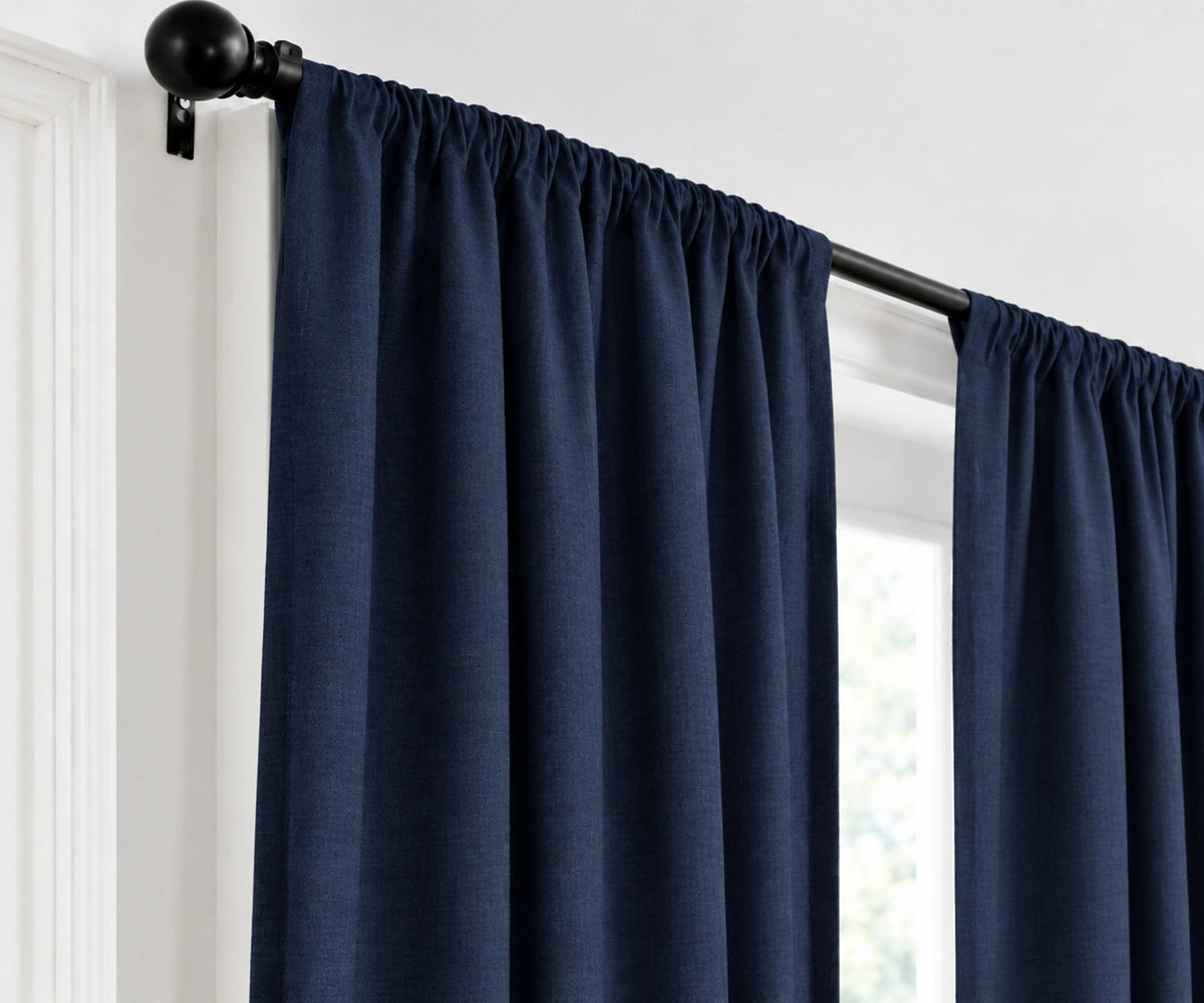 A pair of navy blue curtain panels hanging from a black rod with decorative finials, shown in a real interior setting with a window and white wall visible.