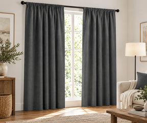 Pair of grey plain cotton curtains hanging on a dark rod in a bright living room.