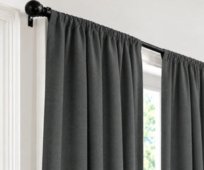 Dark gray curtain panels hanging from a black rod with decorative finials, shown installed on a window in a white interior setting.