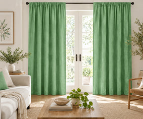 Pair of hunter green plain cotton curtains hanging on a dark rod in a bright living room.