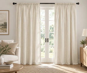Pair of ivory plain cotton curtains hanging on a dark rod in a bright living room.