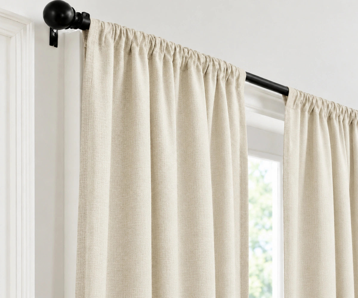 Ivory plain cotton drapes mounted on a dark curtain rod in a brightly lit room.