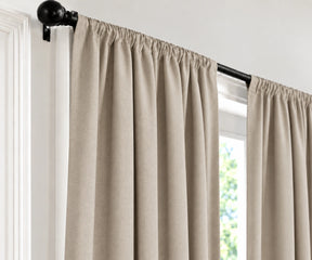 Natural plain cotton drapes mounted on a dark curtain rod in a brightly lit room.