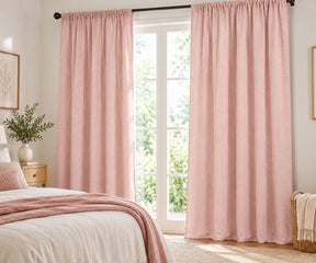 Pair of rose quartz plain cotton curtains hanging on a dark rod in a bright living room.