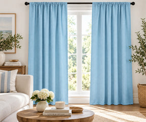 Pair of sky blue plain cotton curtains hanging on a dark rod in a bright living room.