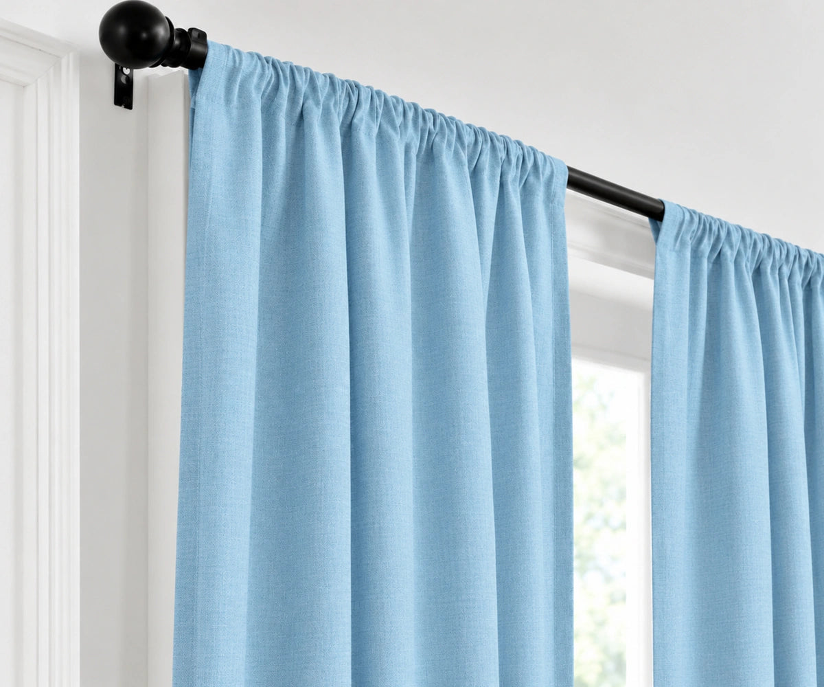 Sky blue plain cotton drapes mounted on a dark curtain rod in a brightly lit room.