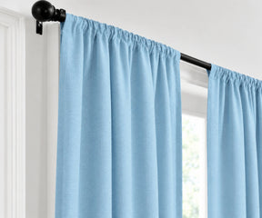 Sky blue plain cotton drapes mounted on a dark curtain rod in a brightly lit room.