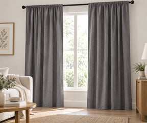 Pair of storm plain cotton curtains hanging on a dark rod in a bright living room.