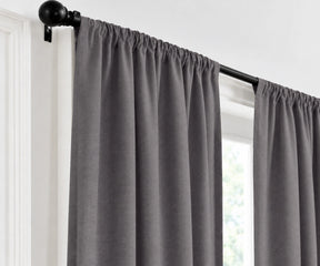 A storm curtain panel hanging from a black rod in a window, shown against a white wall and trim.