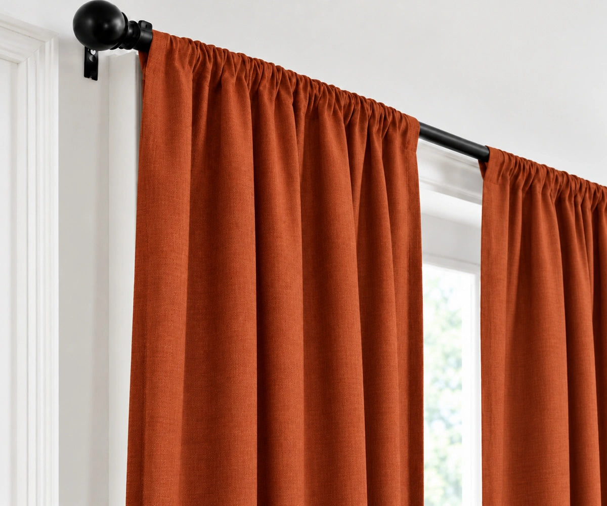 A terracotta curtain panel hanging from a black rod with a black finial, shown in a real interior setting beside a window.