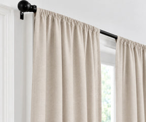 vintage blush curtain panels hanging from a black rod in a bright room with white walls and a window.