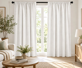 Pair of plain white cotton curtains hanging on a dark rod in a modern bright living room.
