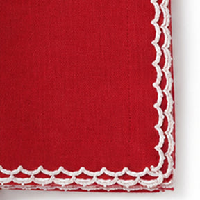 Close-up of a red cotton napkin featuring a white scalloped embroidered edge.