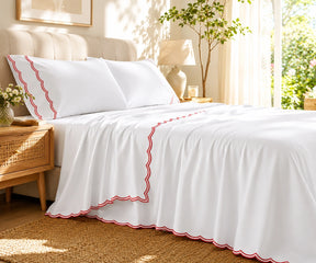 White bed sheet set with vibrant red scalloped embroidery on the pillowcases and flat sheet.