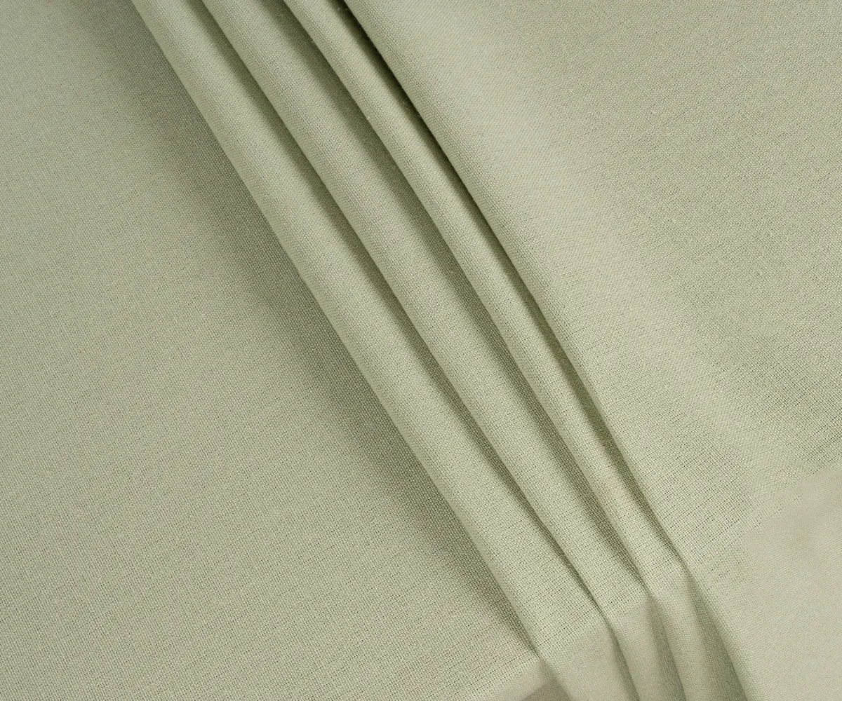 Natural sage green cotton tablecloth neatly spread on a wooden table, paired with neutral runners and rustic tableware for a cozy, stylish tablescape.