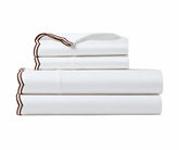 Folded white cotton sheet set with chocolate brown scalloped embroidered trim.