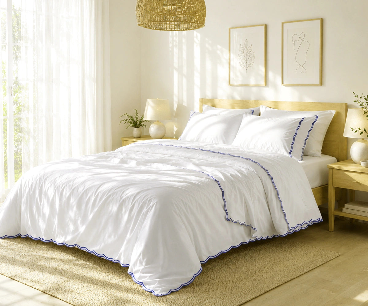 White bed sheet set with navy blue scalloped embroidery on a neatly made bed.
