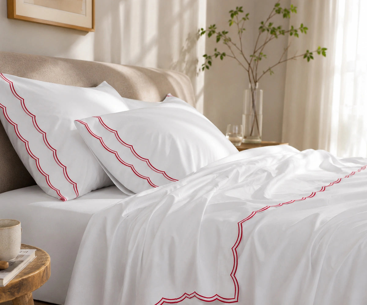 Close-up of white pillowcases and flat sheet featuring a red scalloped embroidered border.