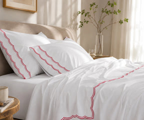 Close-up of white pillowcases and flat sheet featuring a red scalloped embroidered border.