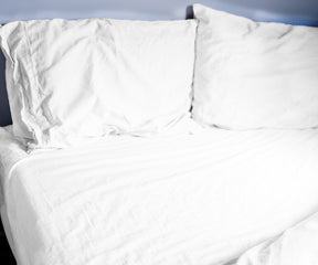 Bed with white cotton fitted sheets, two pillows, and a blanket