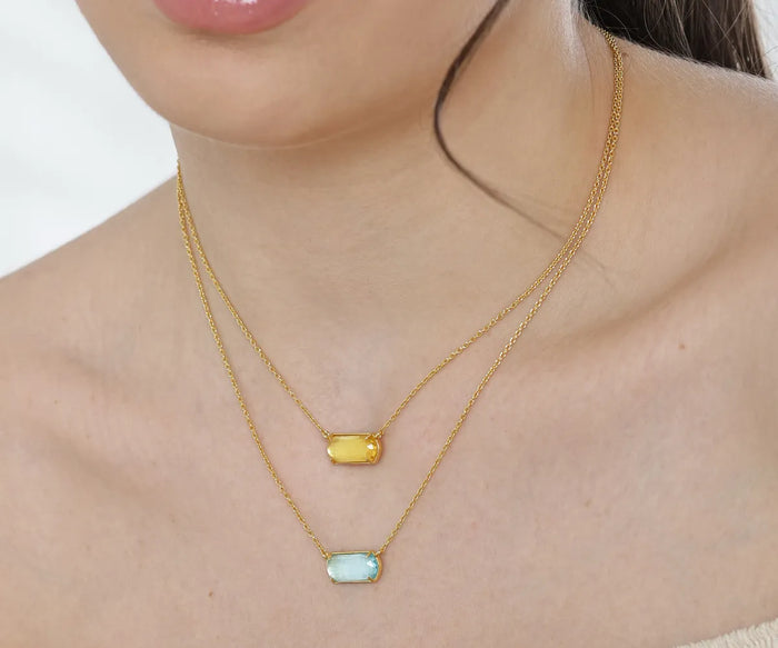 Close-up of a gold chain necklace with a rectangular pendant displayed on a jewelry box, highlighting the necklace's elegant design and fine craftsmanship