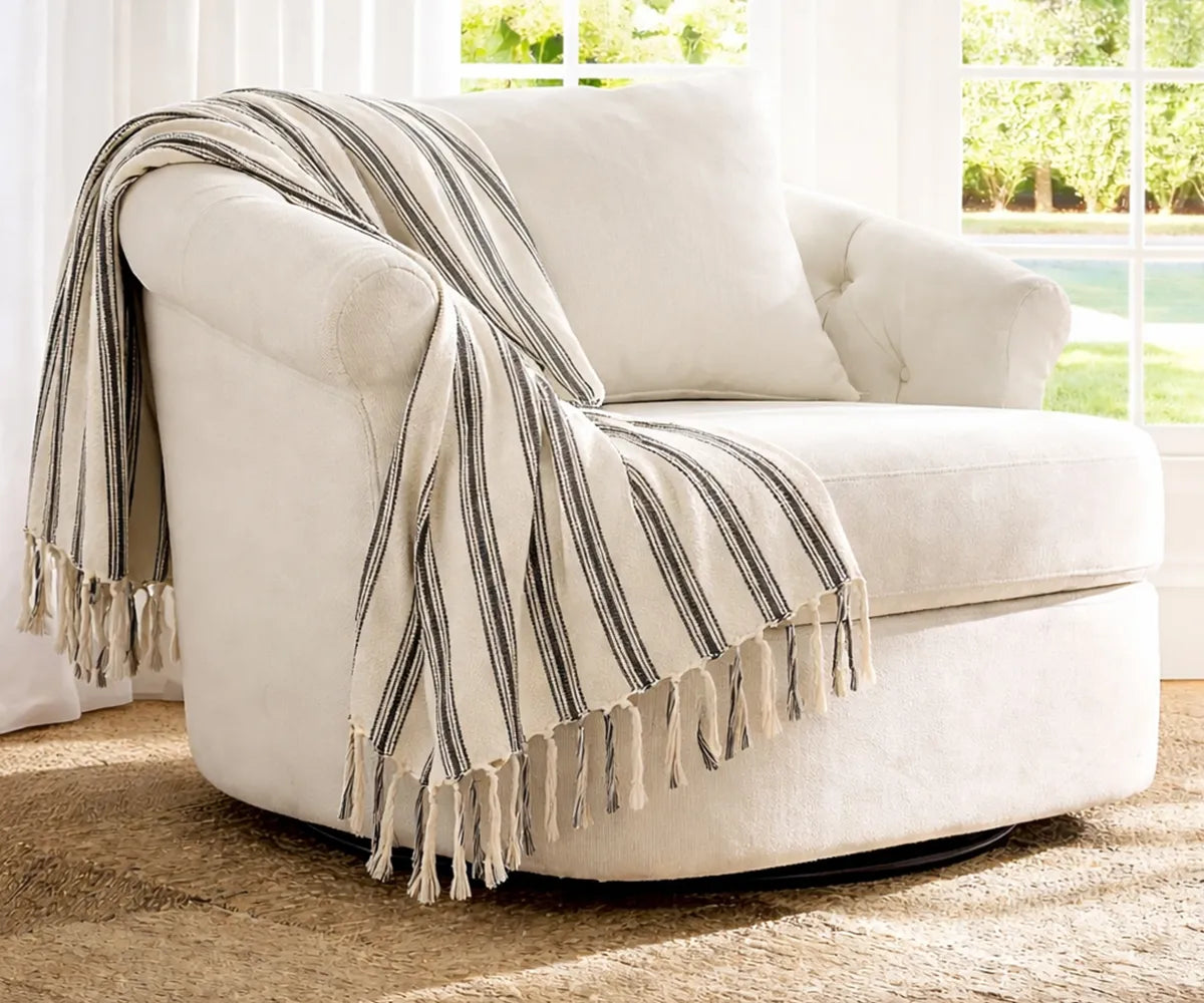 Striped cotton throw blanket with tassel fringe draped over a comfortable living room chair creating a cozy and stylish seating area.