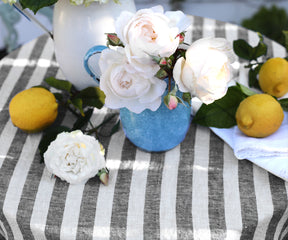 Striped linen tablecloth with white roses, lemons, and a blue vase.