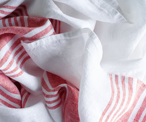 White linen tablecloth with red stripe highlights folded on a bed