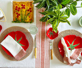 White linen tablecloth on a table set with red and white dishes and greenery