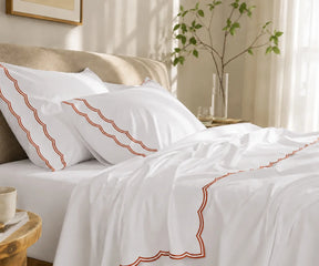 White pillowcases and top sheet with terracotta scalloped embroidered trim on a bed.