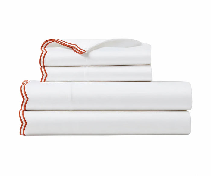 Folded white bed sheet set with terracotta red embroidered borders on a plain white background.