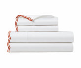 Folded white bed sheet set with terracotta red embroidered borders on a plain white background.