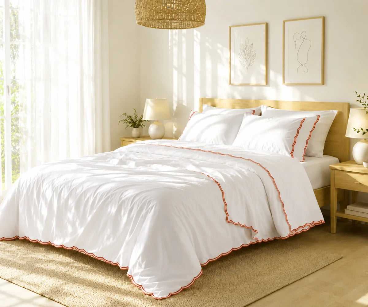 White scalloped bedspread with terracotta embroidery on a bed in a sunlit bedroom.