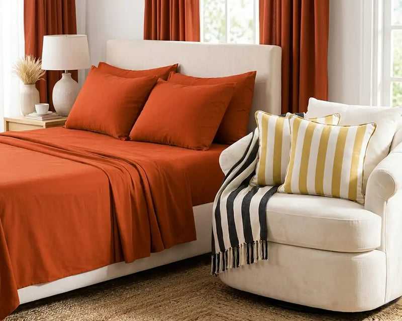 Bedroom with orange bedding and striped pillows on a white bed and chair.