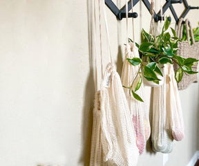 Reusable mesh produce bag with greenery hanging against a white wall
