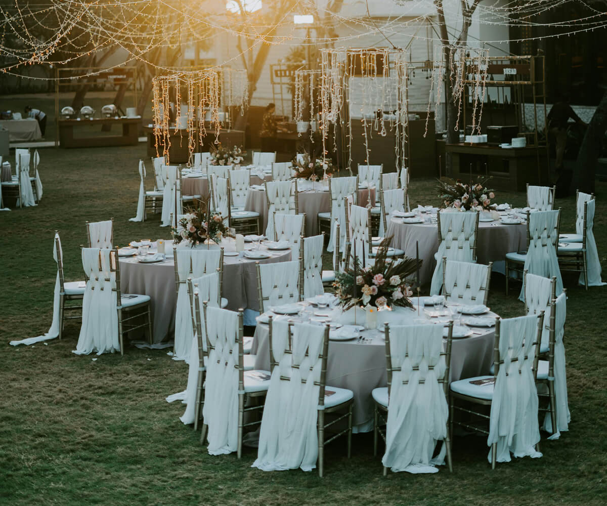 Outdoor wedding reception with round tables, white chair covers, floral centerpieces, and string lights.