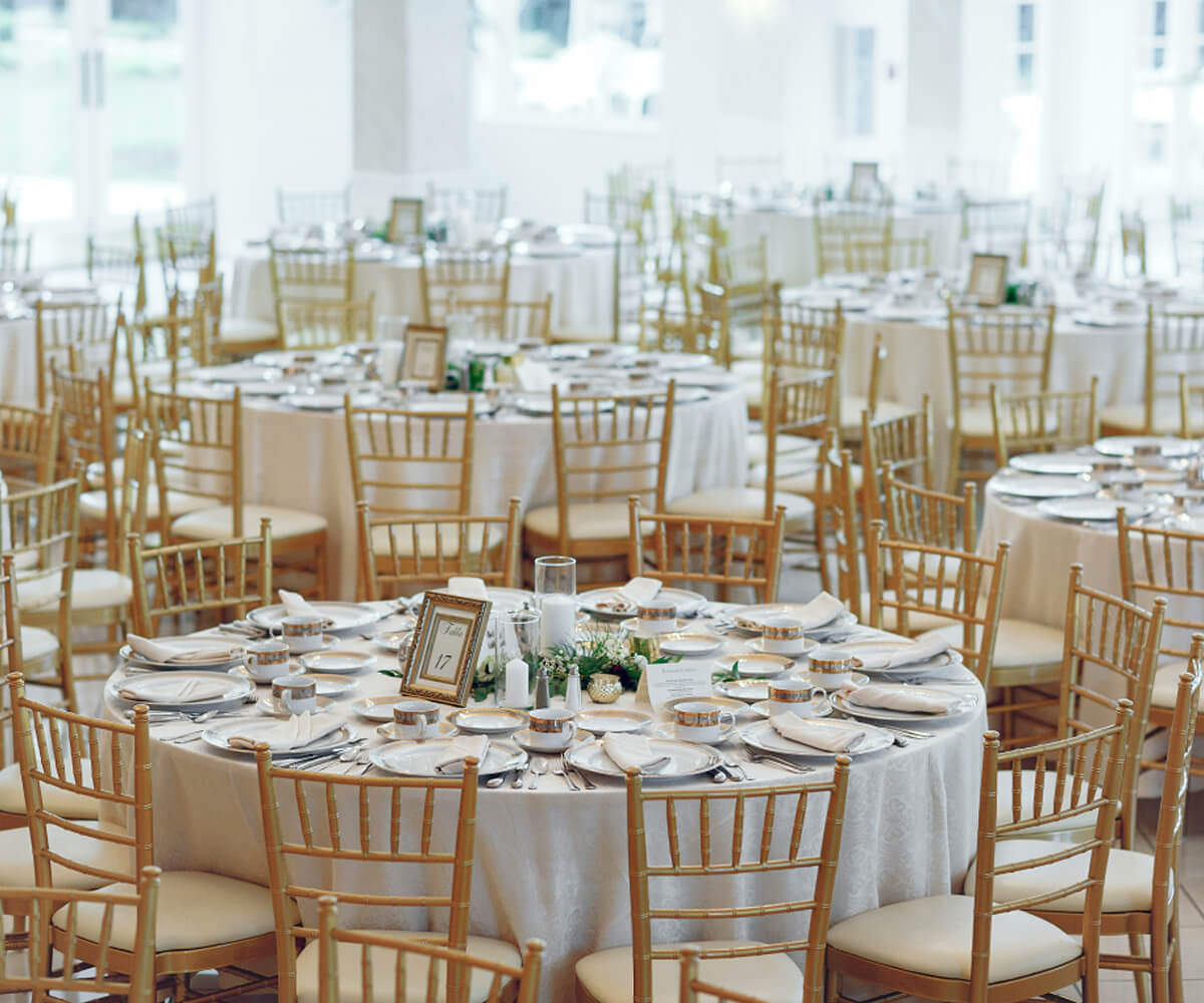 Indoor wedding reception with round tables, gold chairs, and elegant table settings.